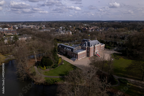 Sideview aerial showing Slot Zeist castle with the moated manor surrounded by green park and urban landscape in the background. Dutch stately venue seen from above.