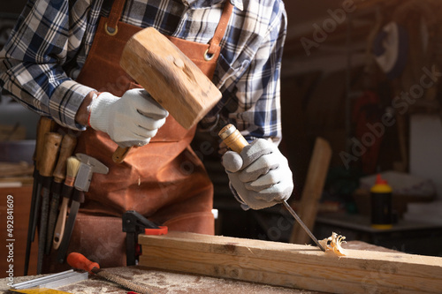 Fotografiet Skilled carpenter carving wood with hammer and chisel