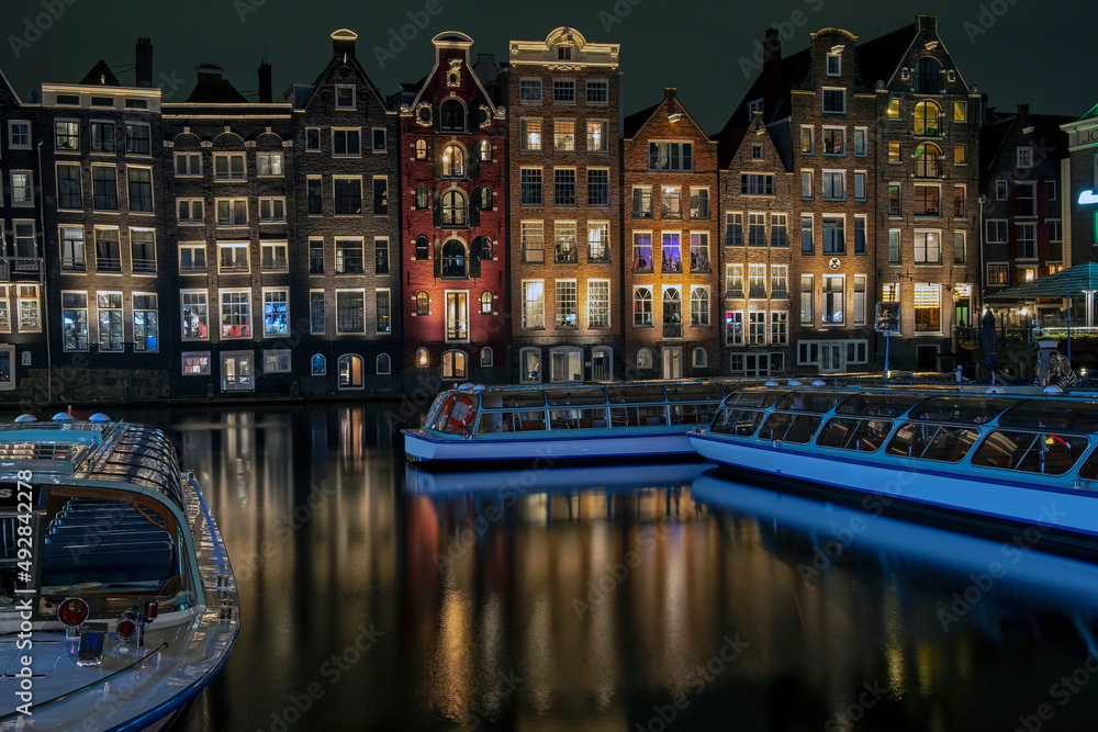 Traditonal houses and cruise boats at the Damrak in Amsterdam in the Netherlands by night