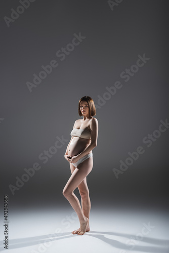 Young pregnant woman in underwear posing on grey background