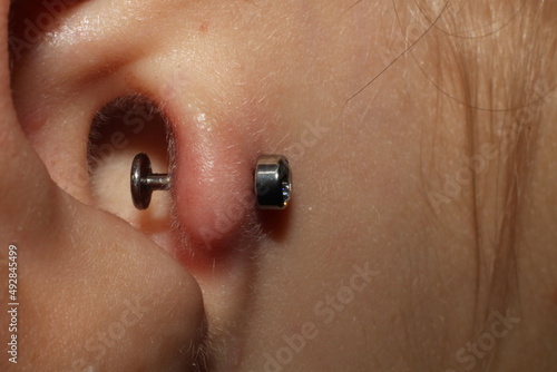 Girl ear piercing. Macro. Tragus piercing + titanium labret with cubic zirconia. Side view. There is a margin for possible swelling of the skin immediately after the puncture.