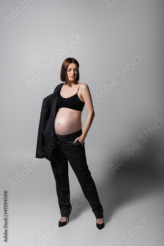 Full length of stylish pregnant model holding jacket on grey background © LIGHTFIELD STUDIOS