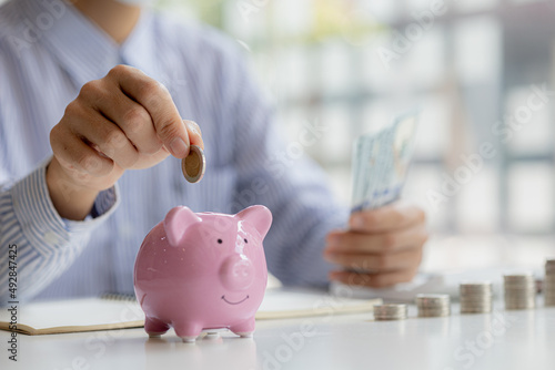 фотографія A businessman is putting coins into a pink pig piggy bank, he is saving for investments, money growth, stock investments