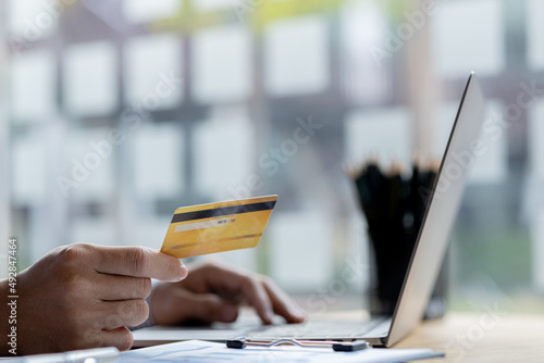A person is holding a credit card to pay online, credit card payments can be used on both laptop computers and mobile phones. Concept of payment for goods and services via credit card.