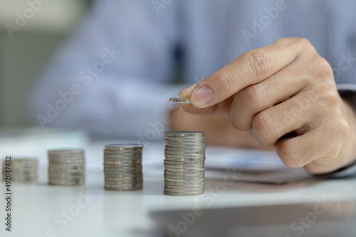 business man is stacking coins on top of the coin pile on the highest row. Placing coins in a row from low to high is comparable to saving money to grow more. Money saving ideas for investing in funds © kamiphotos