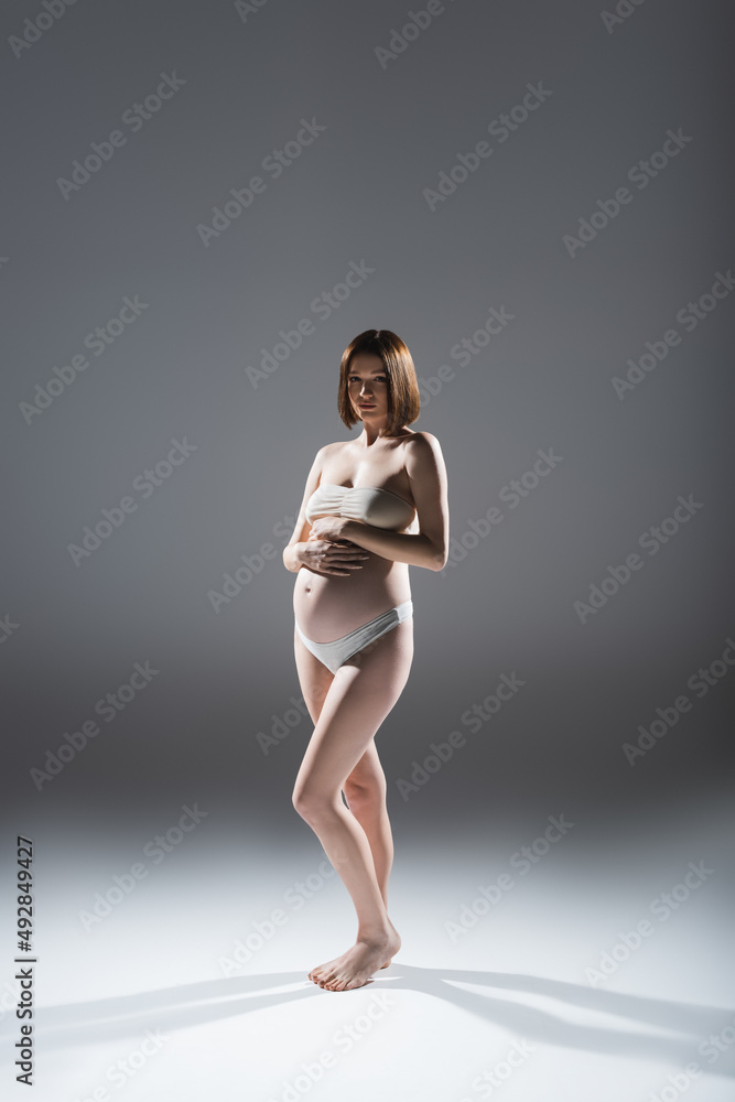 Barefoot pregnant woman in underwear looking at camera on grey background Barefoot pregnant woman in underwear looking at camera on grey background