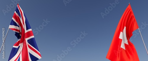 Flags of Great Britain and Switzerland on flagpoles on sides. Flags on a blue background. Place for text. England, London. The United Kingdom. Geneva, Zurich. Commonwealth. 3D illustration.