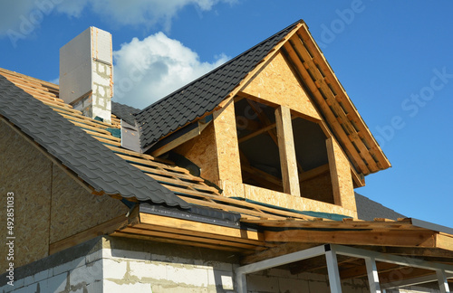 Canvas Print Roofing construction on the stage of metal tiles installation on a gable roof with a dormer using flashing, and unfinished brick chimney