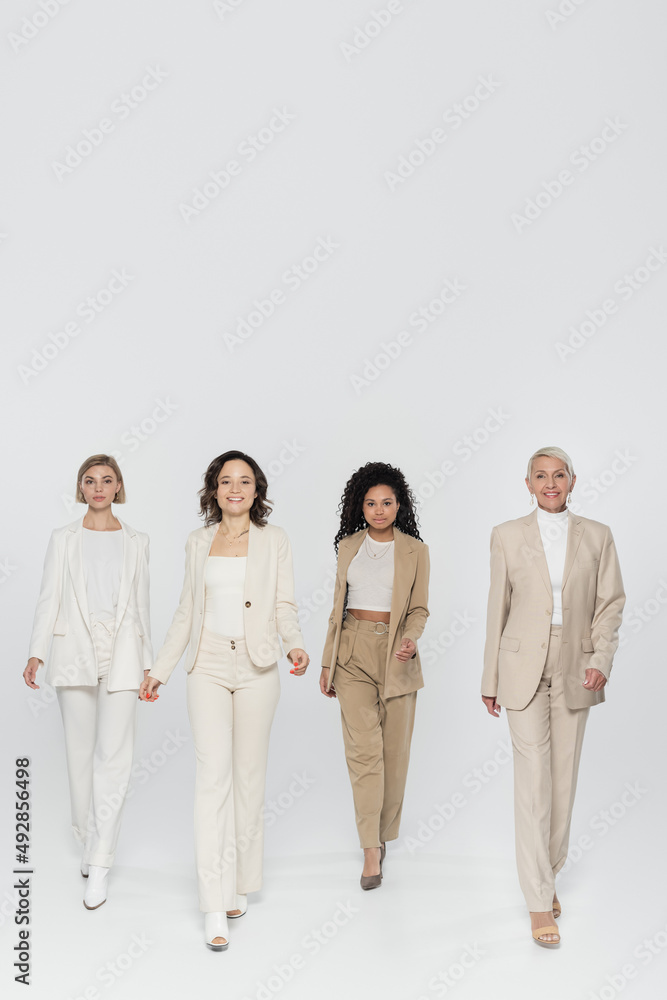 Full length of multiethnic businesswomen walking on grey background, feminism concept. Full length of multiethnic businesswomen walking on grey background, feminism concept.