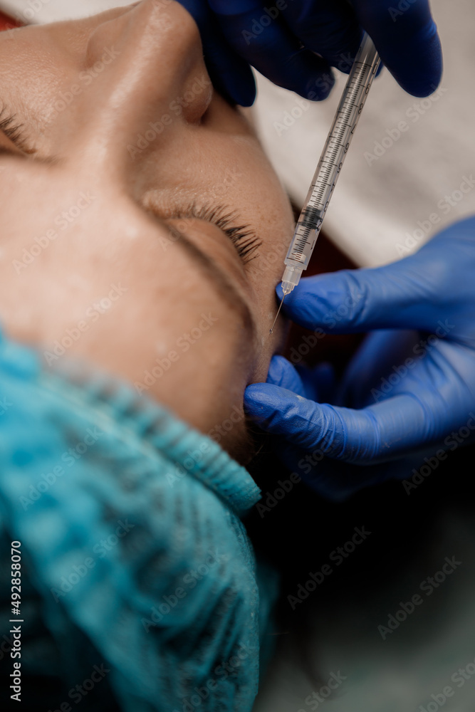 A cosmetologist injects a syringe into a patient, Botox