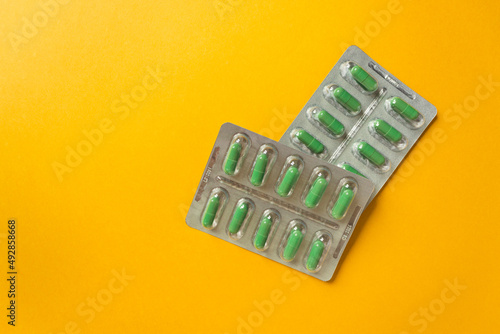 Two silver blisters with supplements and vitamins in green capsules on yellow background. Health care concept.