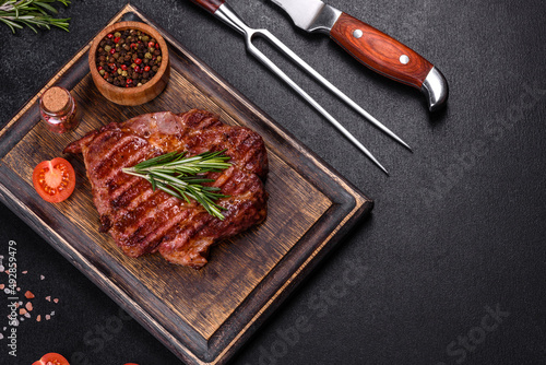Grilled ribeye beef steak, herbs and spices on a dark table