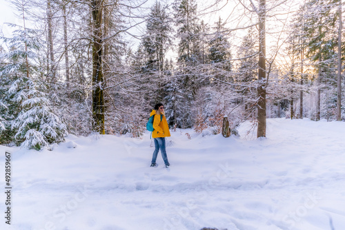 Winterwandern im Winterwald Frau mit gelber Jacke und Rucksack