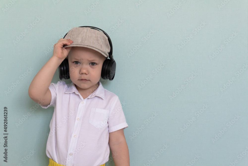 A little boy in a white shirt, yellow shorts and a retro cap listens to music through large headphones. A little boy in a white shirt, yellow shorts and a retro cap listens to music through large headphones.