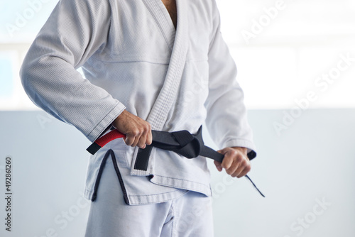Hes an expert. Cropped shot of an unrecognizable male martial artist tying his belt in the gym.