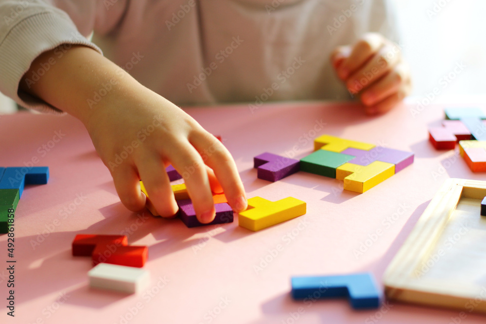Children hands with a colored tangram puzzle on a pink background. everyday children games, wooden eco-friendly toys for children leisure Children hands with a colored tangram puzzle on a pink background. everyday children games, wooden eco-friendly toys for children leisure