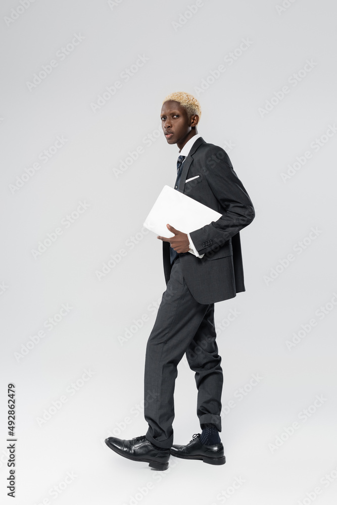 full length of blonde african american businessman in suit holding laptop on grey full length of blonde african american businessman in suit holding laptop on grey