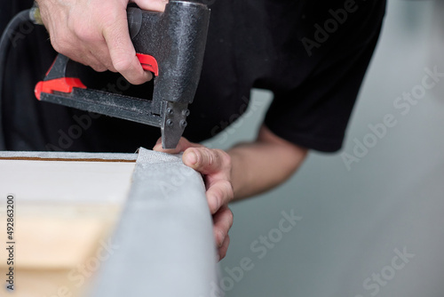 Production of upholstered cabinet furniture. Worker qualitatively fixes the fabric with a pneumatic stapler on the body in the factory shop.  photo