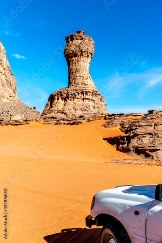 World cup naturally shaped stone rock and 4x4 vehicle front part. Sahara Desert of Tadrart Rouge, Djanet, Algeria. Offroad car looking at Rocky Mountains and a rock with the shape of a rook. Blue sky. photo