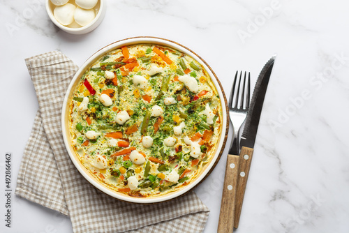 Egg frittata omelet with seasonal vegetables and cheese in plate on white marble background. Top view healthy diet food concept