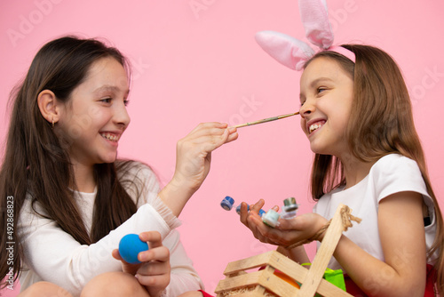 Close up photo of lovely girls making fun painting nose and wearing bunny ears  preparing for theEaster holiday.