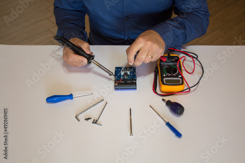 Photo of the hands of a man using a soldering iron to repair a battery pack electrical board. Homemade repair work photo
