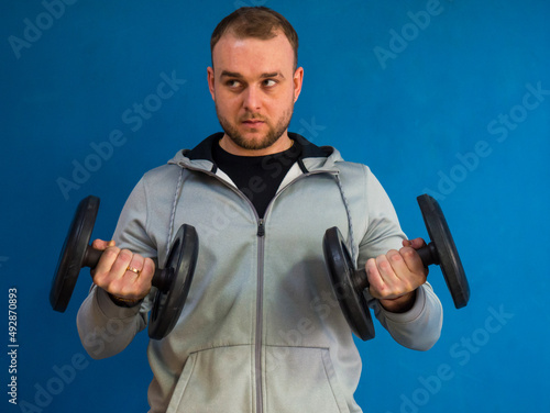 Young active strong man training biceps muscles with heavy dumbbell weight in the gym