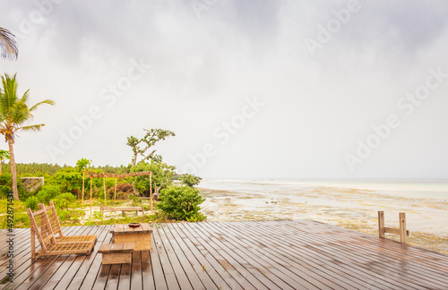 Empty wooden terrace with lounge beds and table on ocean coast. Wooden patio after rain. Wet terrace in tropical resort, low tide. Backyard in summer tourist resort. Travel in Africa.  © Nataliia