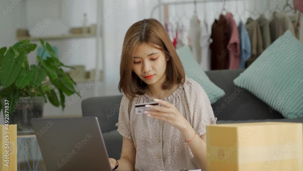 Asian woman receive phone call for order. Business girl talk to client on cellphone use laptop discuss deal, millennial woman sit at desk at home look at computer screen makes order. Asian woman receive phone call for order. Business girl talk to client on cellphone use laptop discuss deal, millennial woman sit at desk at home look at computer screen makes order.