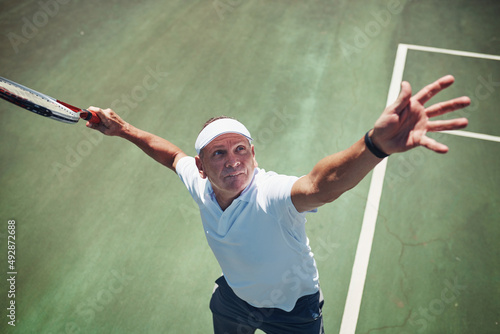 Ready, set, go. High angle shot of a handsome mature sportsman playing tennis alone on a court during the day.