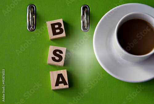 BSA - acronym on wooden cubes against the background of a green folder and a cup of coffee