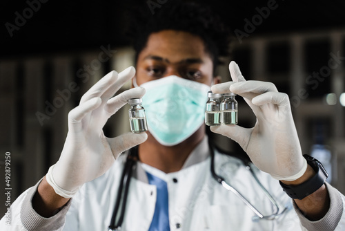 Black doctor with 3 doses of vaccine. Booster vaccination. African doctor in medical mask is holding vaccines in hand.