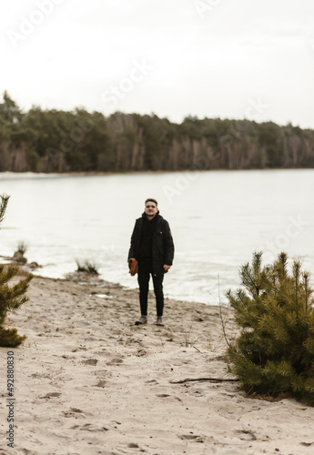 Man standing on the shore on a sandy beach on a background of trees in black clothes and smiling
