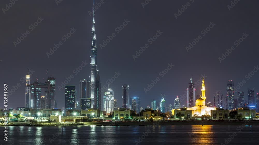 Modern Dubai city skyline timelapse at night with illuminated skyscrapers over water surface