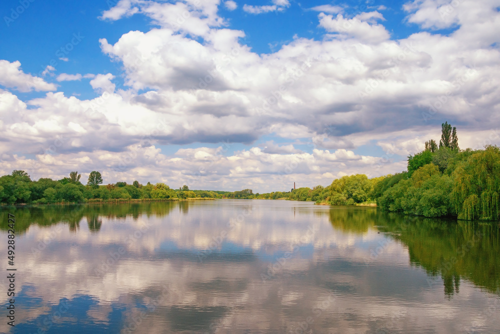 Clouds ans green trees are reflected in water of lake. Beautiful peaceful Ukrainian landscape. Ukraine, Uman, Ostashivskiy lake
