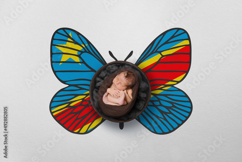 Tiny baby portrait with wings in color of national flag. Newborn photography concept. Democratic Republic of the Congo