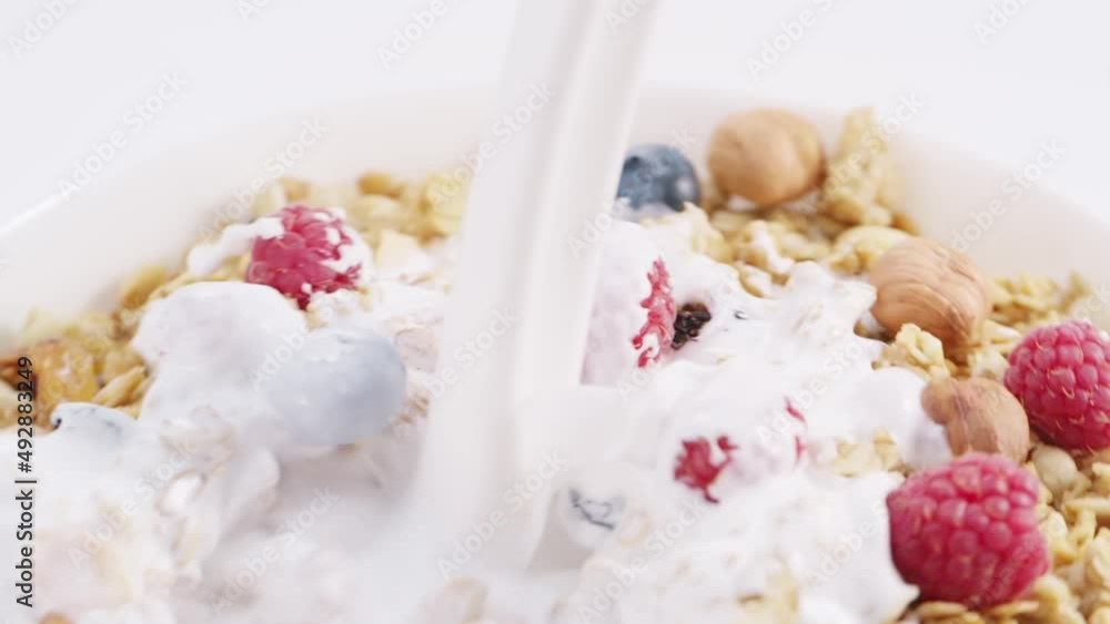 Milk flow pouring into the white rotating bowl with healthy muesli, cornflakes, berries, fruits and nuts Milk flow pouring into the white rotating bowl with healthy muesli, cornflakes, berries, fruits and nuts