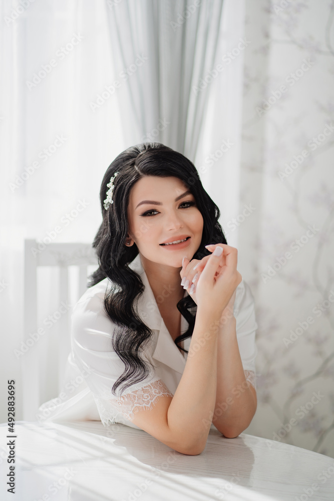 brunette bride in white silk pajamas with styling and makeup at the table brunette bride in white silk pajamas with styling and makeup at the table
