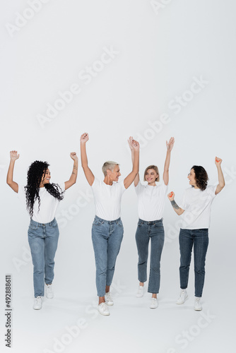 Positive multiethnic women raising hands on grey background, feminism concept.