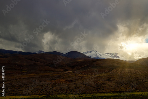 Sun peeks through clouds over snowy hills in Salta, Argentina