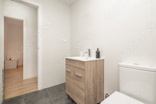 bathroom with white porcelain toilets  white walls  wooden furniture and dark stoneware floors