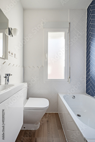 Toilet with white lacquered furniture  bathtub wall with blue tiles and the rest at half height in white