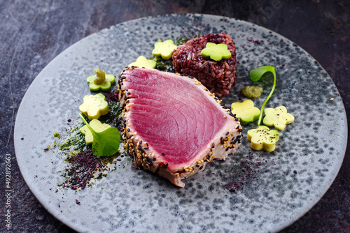 Modern style traditional Japanese gourmet seared tuna fish steak tataki with Sakura avocado, portulak salat and mixed red brown rice served as close-up on a Nordic design plate photo
