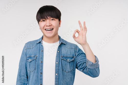 Smiling with braces asian korean man boy student showing okay gesture isolated in white background. Stomatology, dentistry concept photo