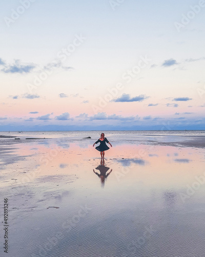 Silhueta de mulher de vestido refletida na àgua durante pôr do sol na praia em Tatuamunha, Alagoas