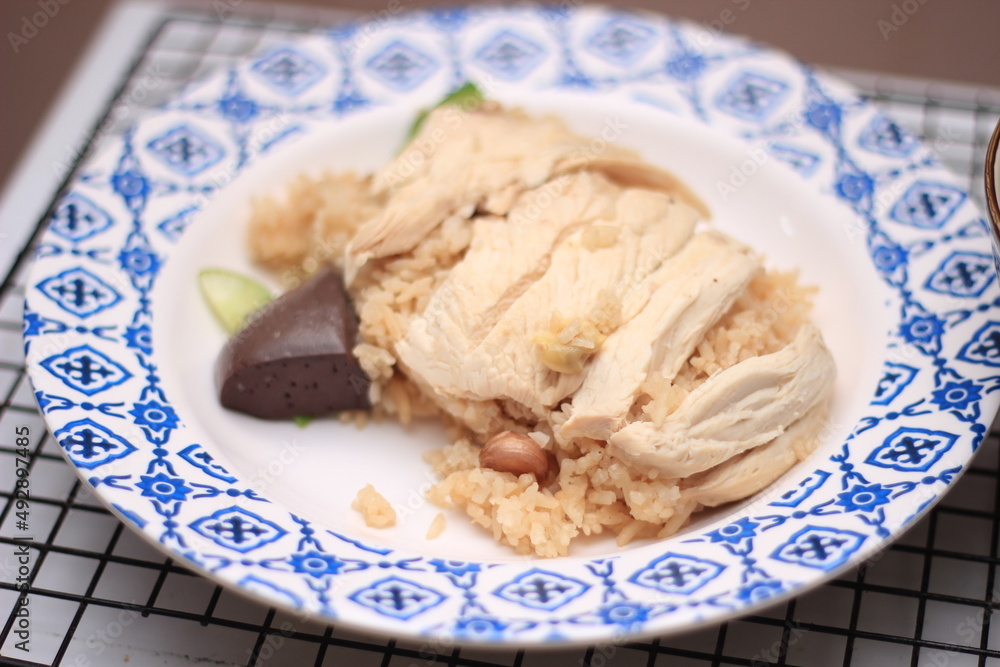 Chicken rice and boiled chicken served in a white plate with blue stripes.
