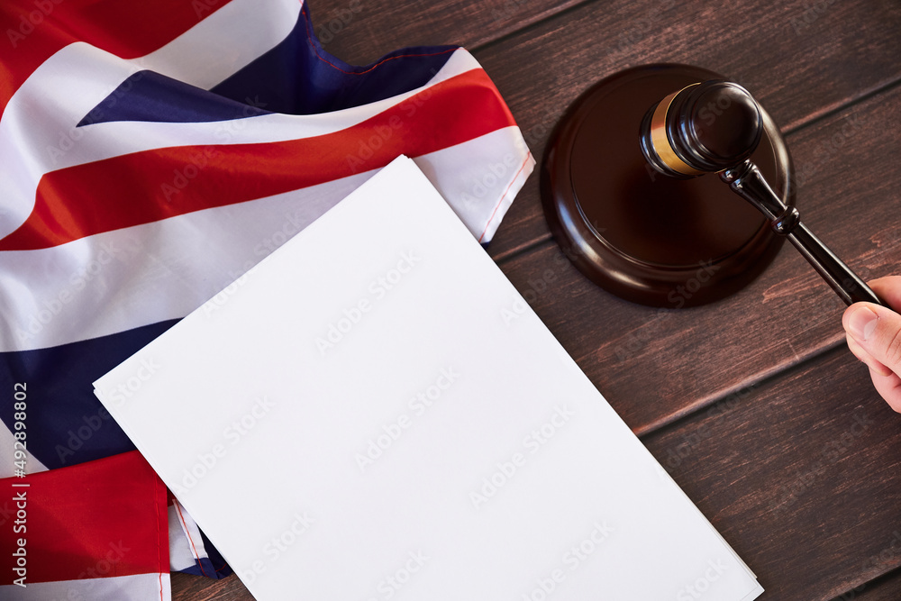 Fototapeta premium Gavel in judges hand, United Kingdom flag, blank list on wooden table. Law and justice concept.