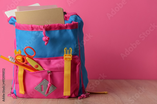 Stylish backpack with stationery on table against color background