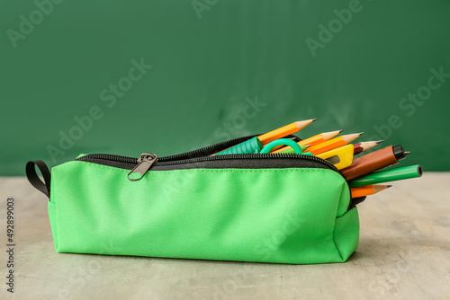 Green pencil case with stationery on table in classroom