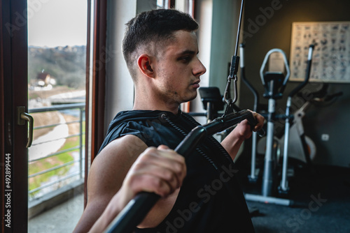 One man young adult caucasian male amateur bodybuilder training back on the cable machine in the gym wearing shirt real people copy space side view